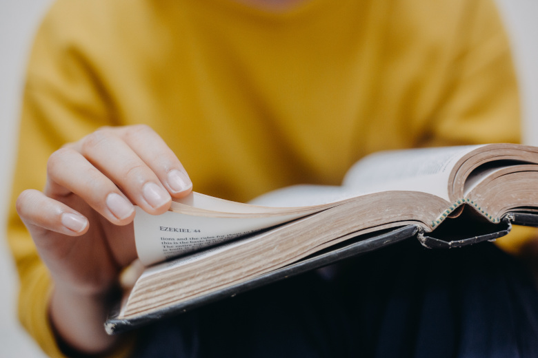 Person in gelbem Oberteil blättert in einer aufgeschlagenen Bibel.